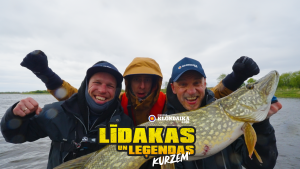 Trīs priecīgi vīrieši laivā, rokās turot lielu, tikko noķertu līdaku. Attēlam ir uzlikts teksts: "LĪDAKAS UN LEĢENDAS KURZEM".