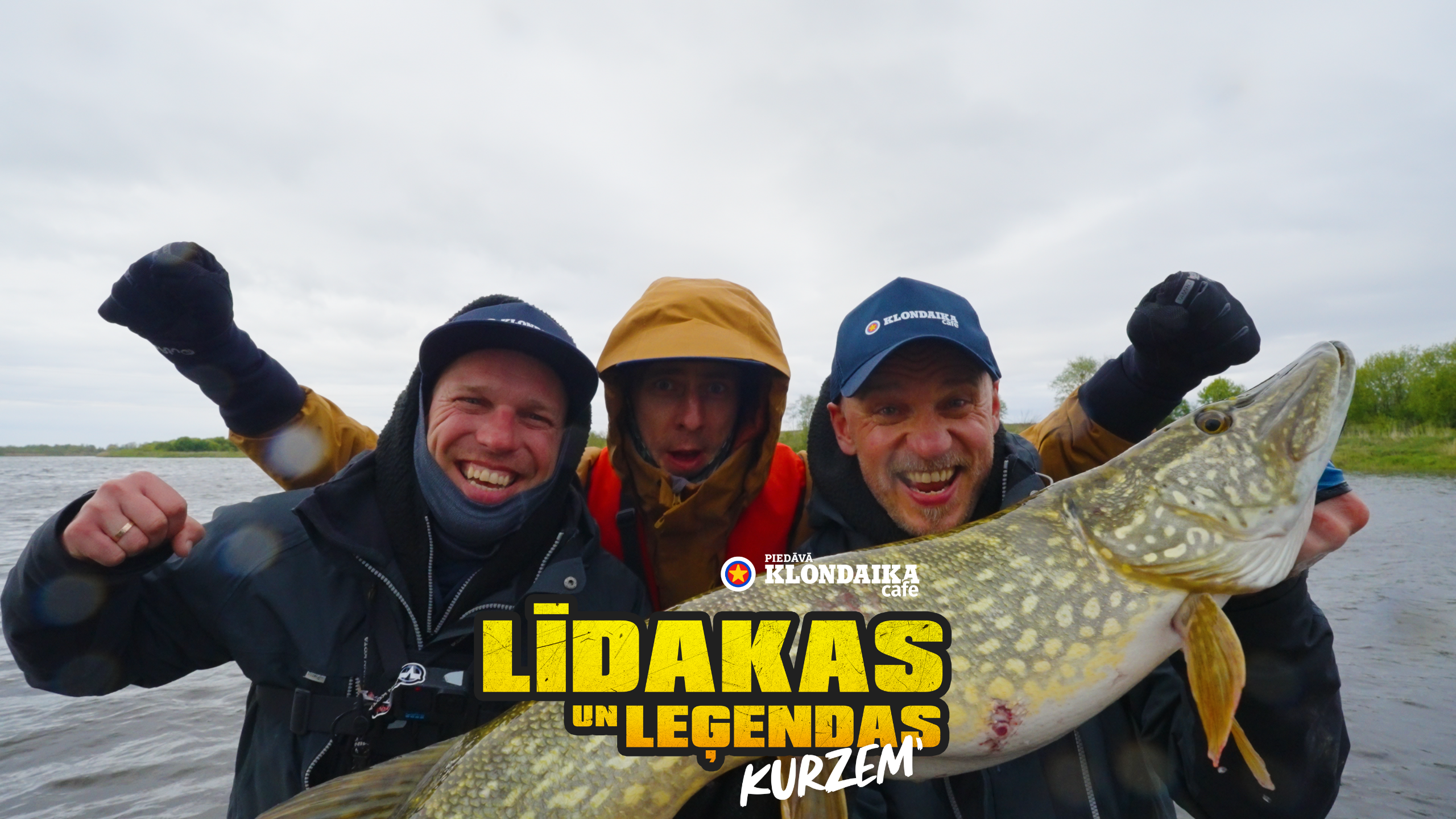Trīs priecīgi vīrieši laivā, rokās turot lielu, tikko noķertu līdaku. Attēlam ir uzlikts teksts: 