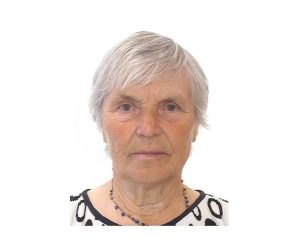 Gados vecāka sieviete ar īsiem sirmiem matiem skatās kamerā
