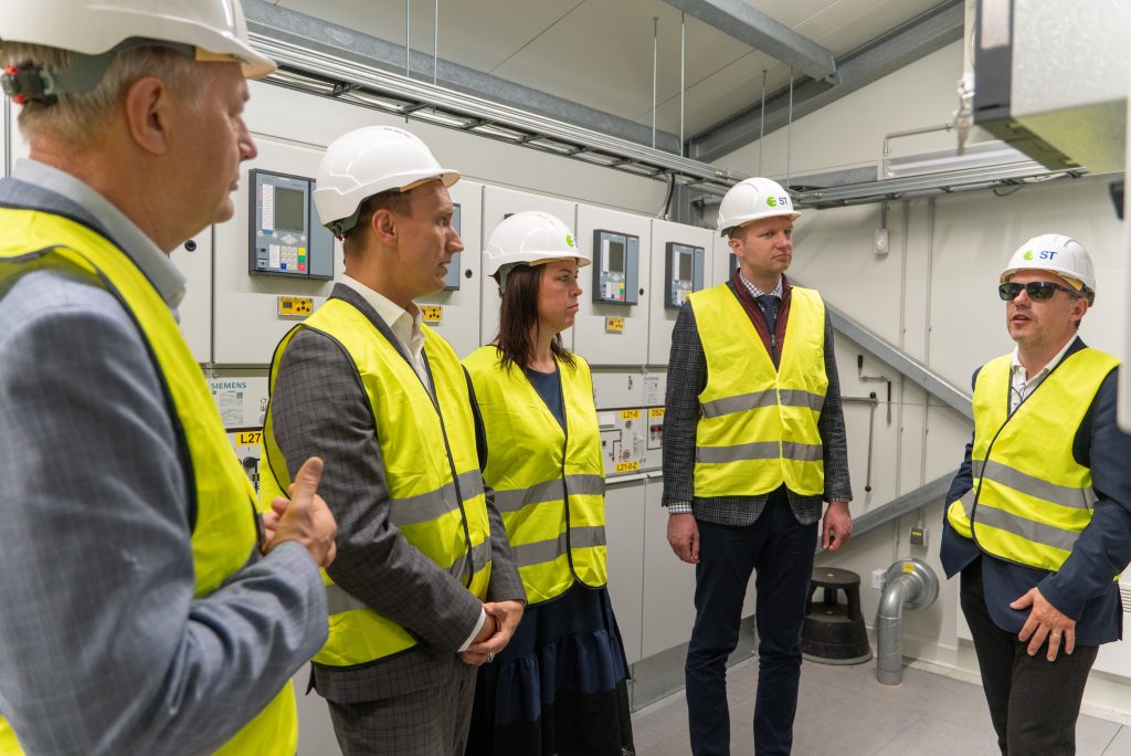 Pieci cilvēki apskata elektriskās iekārtas apakšstacijā.