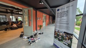 Apavi pie durvīm un plakāts par kopīgo maģistra programmu dizainā