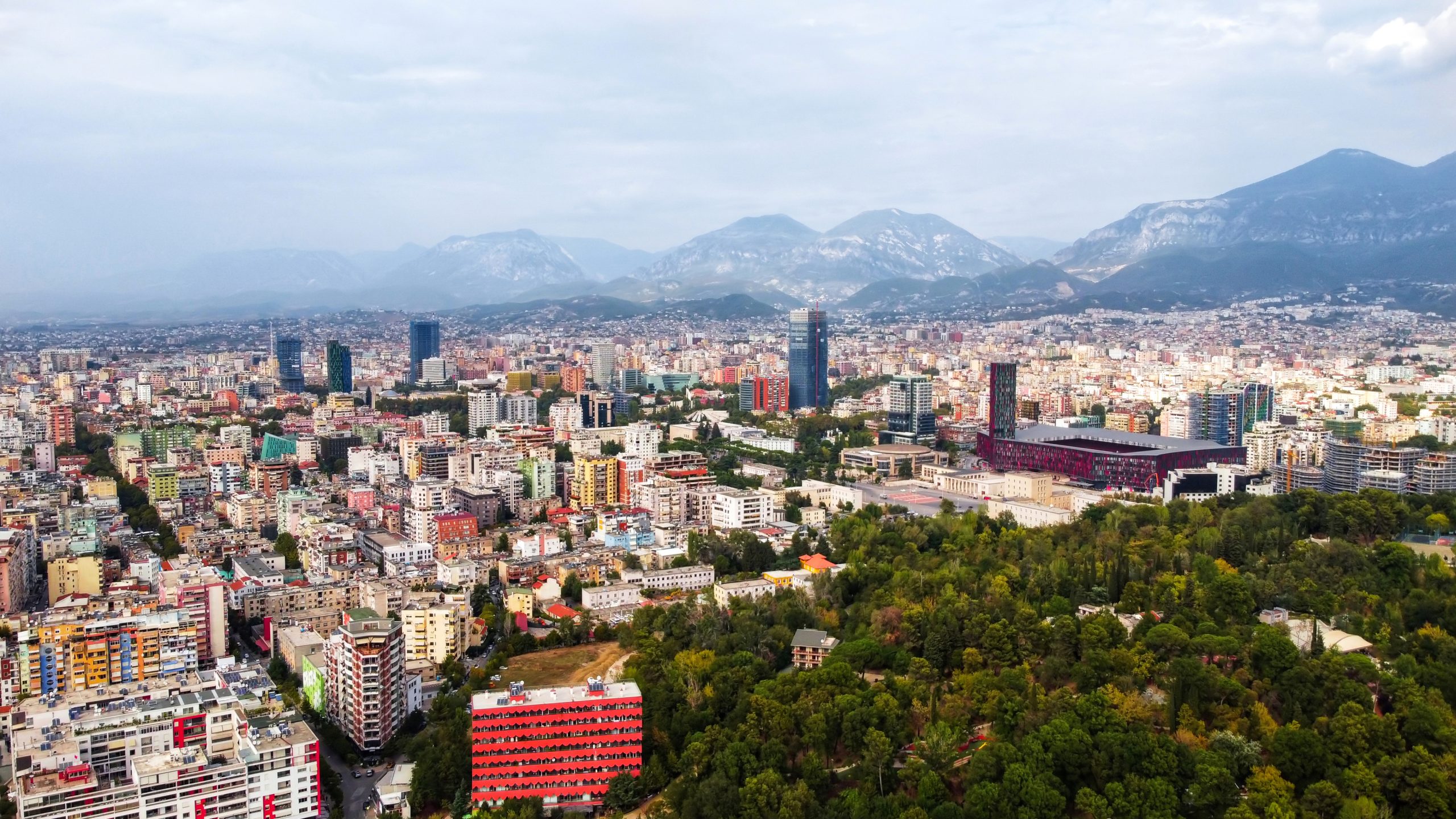 Lielpilsētas panorāma ar augstceltnēm un kalniem fonā.