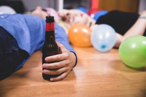 Pēc ballītes draugi guļ uz grīdas, blakus ir alus pudele