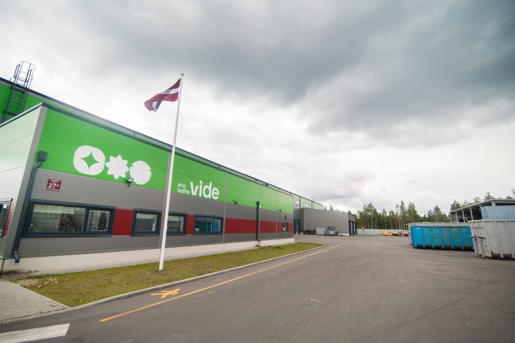 AS “Eco Baltia vide” ēka ar zaļi-pelēku fasādi, sarkanu joslu un Latvijas karogu vējā.