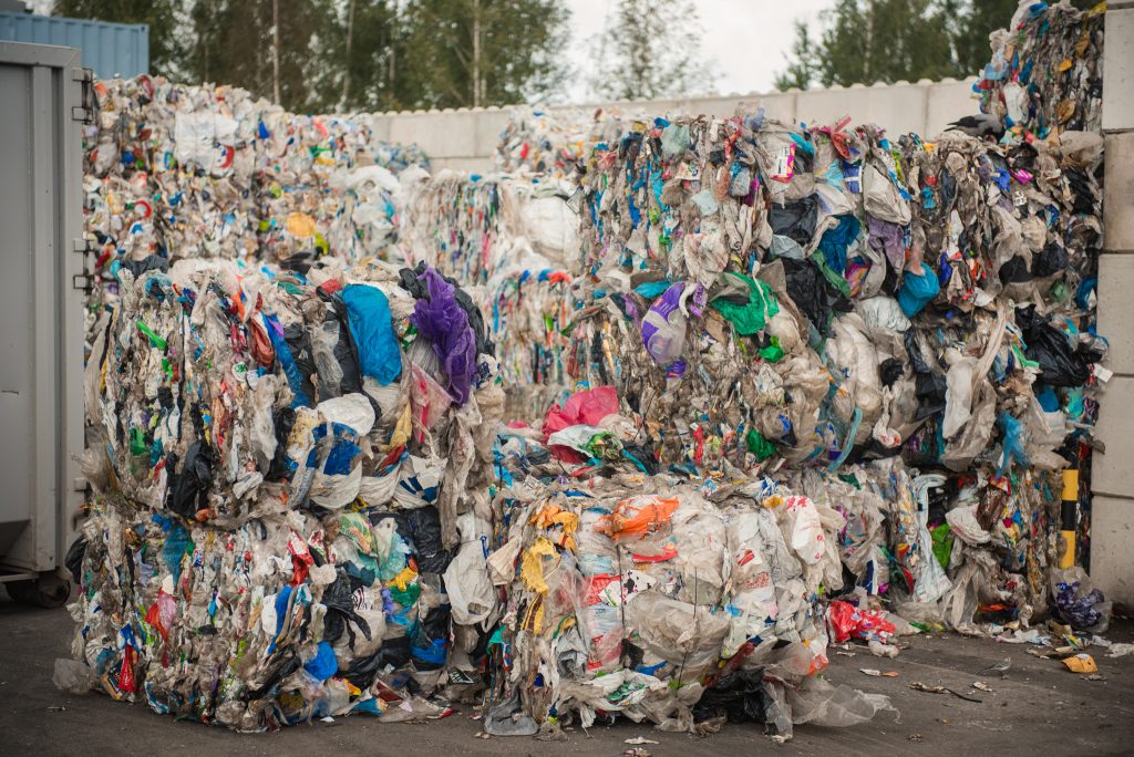 Lieli, sapresēti un sasieti polietilēna un cita plastmasas atkritumu bloki atkritumu šķirošanas laukumā.