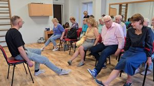 Seniori vingrošanas nodarbībā sēžot uz krēsliem