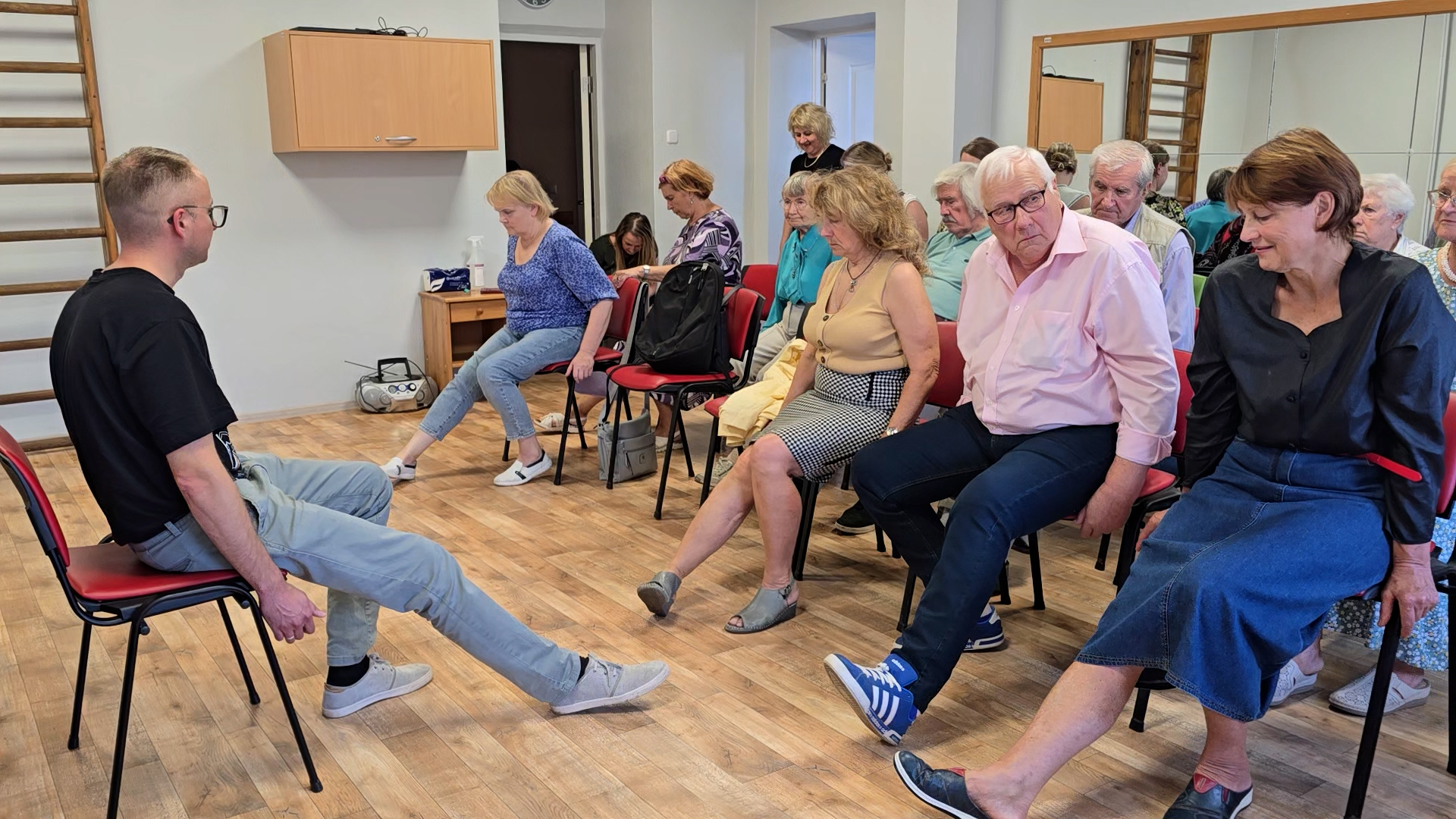 Seniori vingrošanas nodarbībā sēžot uz krēsliem