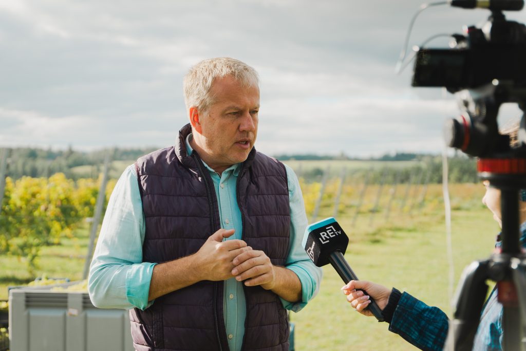 Abavas vīna darītavas saimnieks Mārtiņš Barkāns vīna dārzā sniedz interviju "ReTV" žurnālistam, turot rokas kopā.