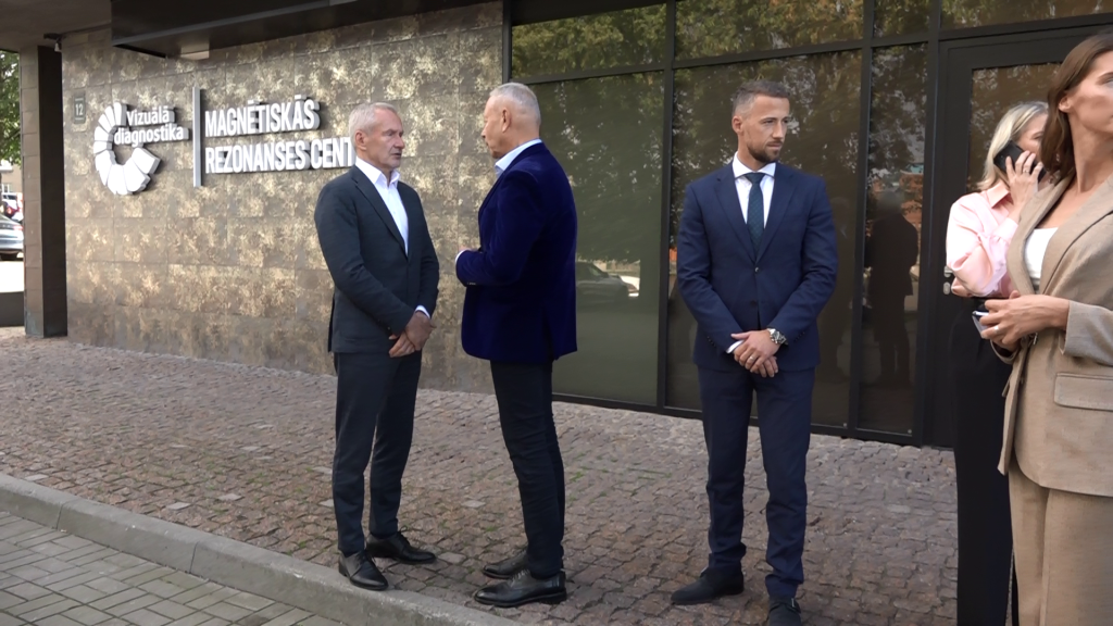 Grupa cilvēku stāv pie ēkas, kurā atrodas magnētiskās rezonanses centrs.