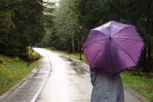 Sieviete ar violetu lietussargu pastaigājas pa meža ceļu lietus laikā