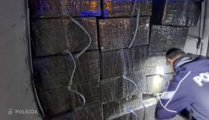 Policijas darbinieks pārbauda lielu daudzumu melnos plēvē ietītu iepakojumu.