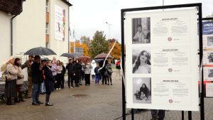 Cilvēki ar lietussargiem apmeklē izstādes “Nesaņemtie diplomi” atklāšanu Valmierā, pie Vidzemes Augstskolas ēkas.