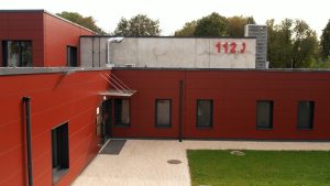 Katastrofu pārvaldības centra ēka ar sarkanu fasādi un uzrakstu “112” uz jumta.