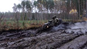 Karavīri ar sešriteņu visurgājēju pārvietojas pa dubļainu meža ceļu militāro mācību laikā