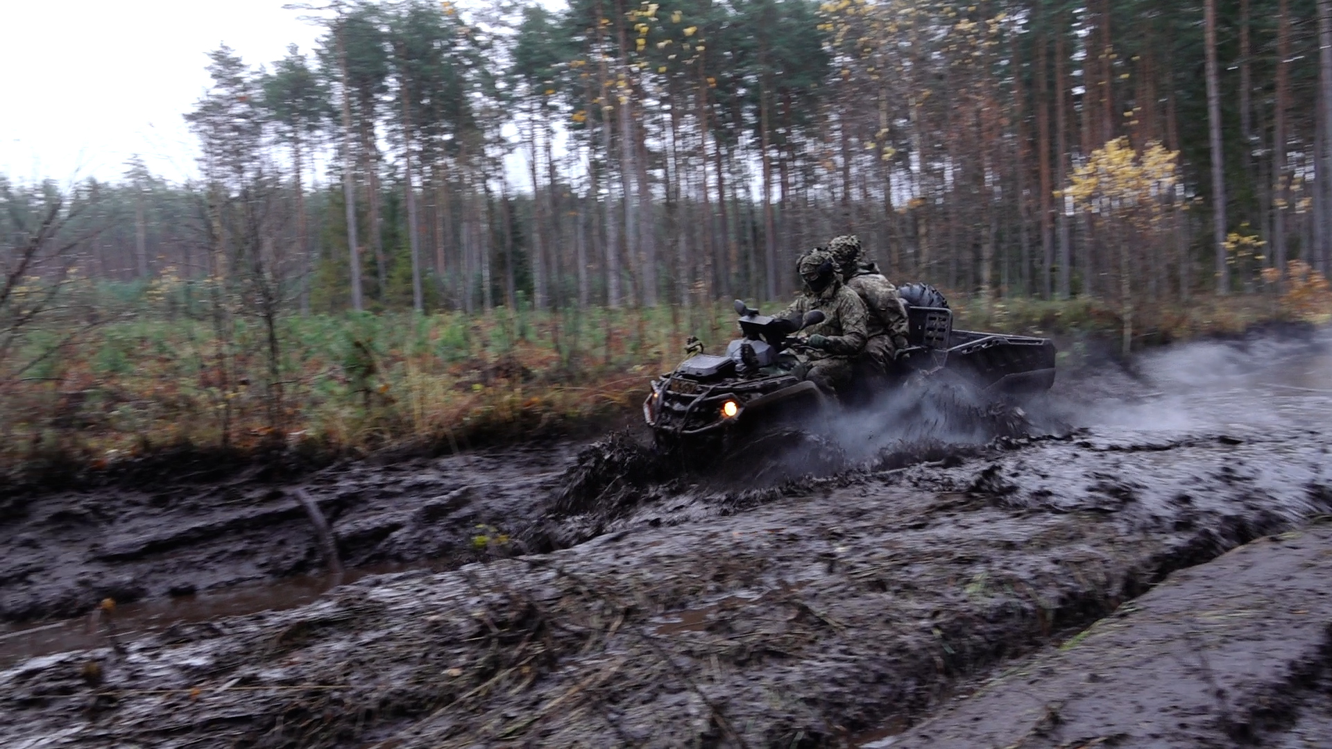 Karavīri ar sešriteņu visurgājēju pārvietojas pa dubļainu meža ceļu militāro mācību laikā