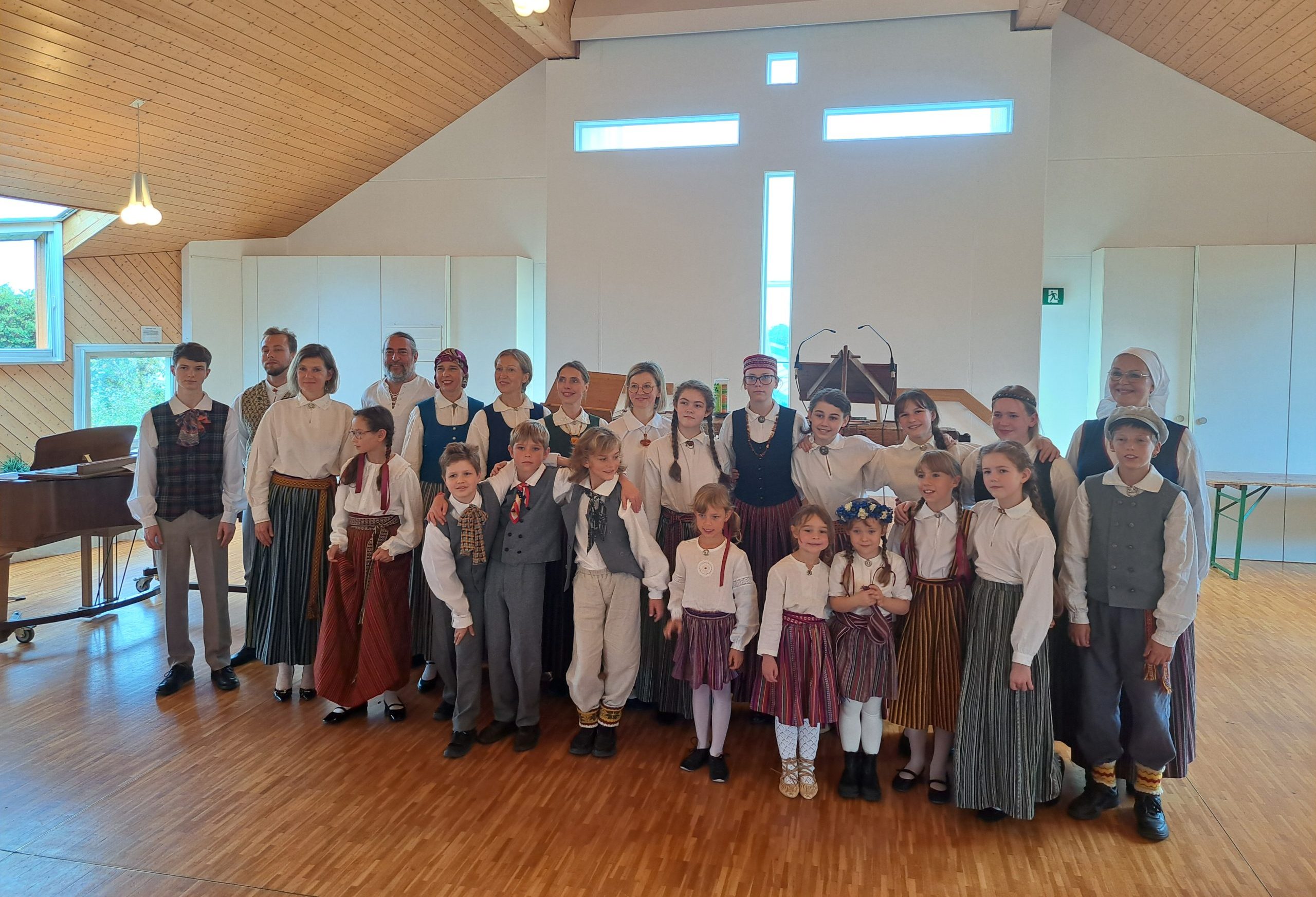 Eiropas bērnu un jauniešu kora dalībnieki, ģērbti latviešu tautas tērpiem stilizētos tērpos, stāv kopīgā fotogrāfijā pēc koncerta Ženēvā, Šveicē.