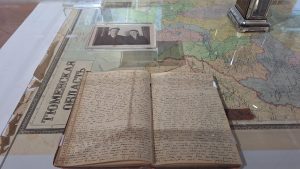 Vēsturiska dienasgrāmata un melnbalta fotogrāfija uz Tjumeņas apgabala kartes muzeja izstādē.