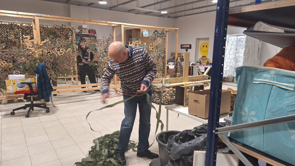 Vīrietis pin maskēšanās tīklu Ukrainas armijai biedrībā "Tavi draugi".