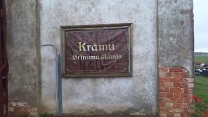Izkārtne ar uzrakstu “Krāmu Brīnumu šķūnis” uz vecas ēkas sienas