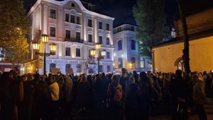 Liels cilvēku pūlis nakts piketā pie Saeimas, redzama vēsturiskā ēka un ielu laternas.