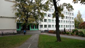 Skolas ēka ar skolēnu un velosipēdiem pie ieejas rudens dienā.
