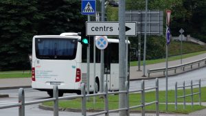 Balts autobuss ar uzrakstu “VTU Valmiera” brauc pilsētā pie ceļa zīmes “centrs”.