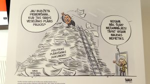 Karikatūra, kur politiķis meklē sirds veselības plānu dokumentu kalnā ar uzrakstu “Politikas plānošanas dokumenti”, bet kolēģe no durvīm sauc, ka tāpat visam naudas nepietiks.