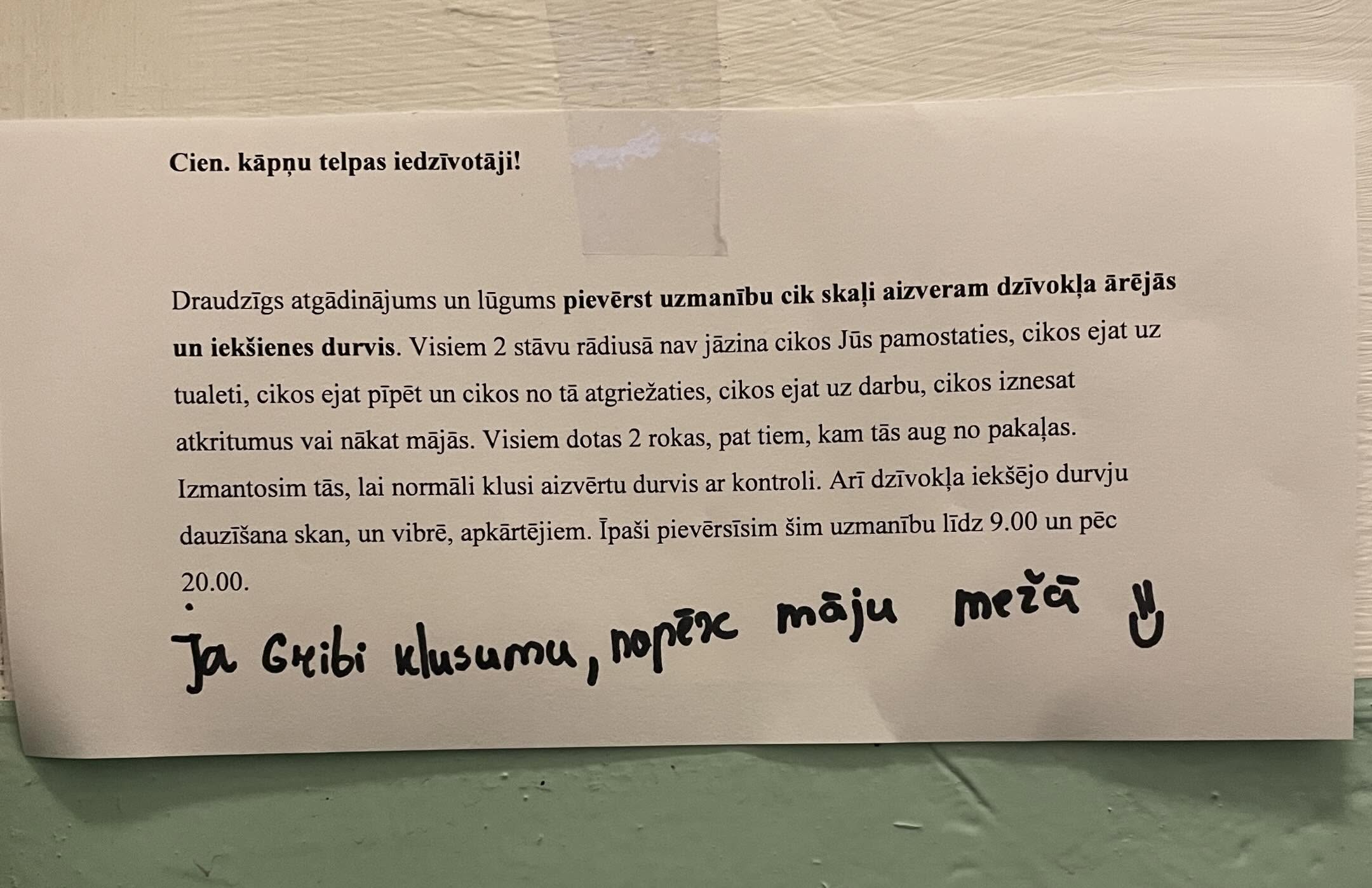 Paziņojums uz papīra lapas, kas pielīmēts pie sienas, ar tekstu latviešu valodā par lūgumu klusi aizvērt dzīvokļa ārdurvis un iekšdurvis, kā arī ar rokas piezīmi apakšā: 