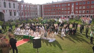 Liels studentu pūlis Jelgavas pils pagalmā veic sinhronizētu priekšnesumu uz zālāja.