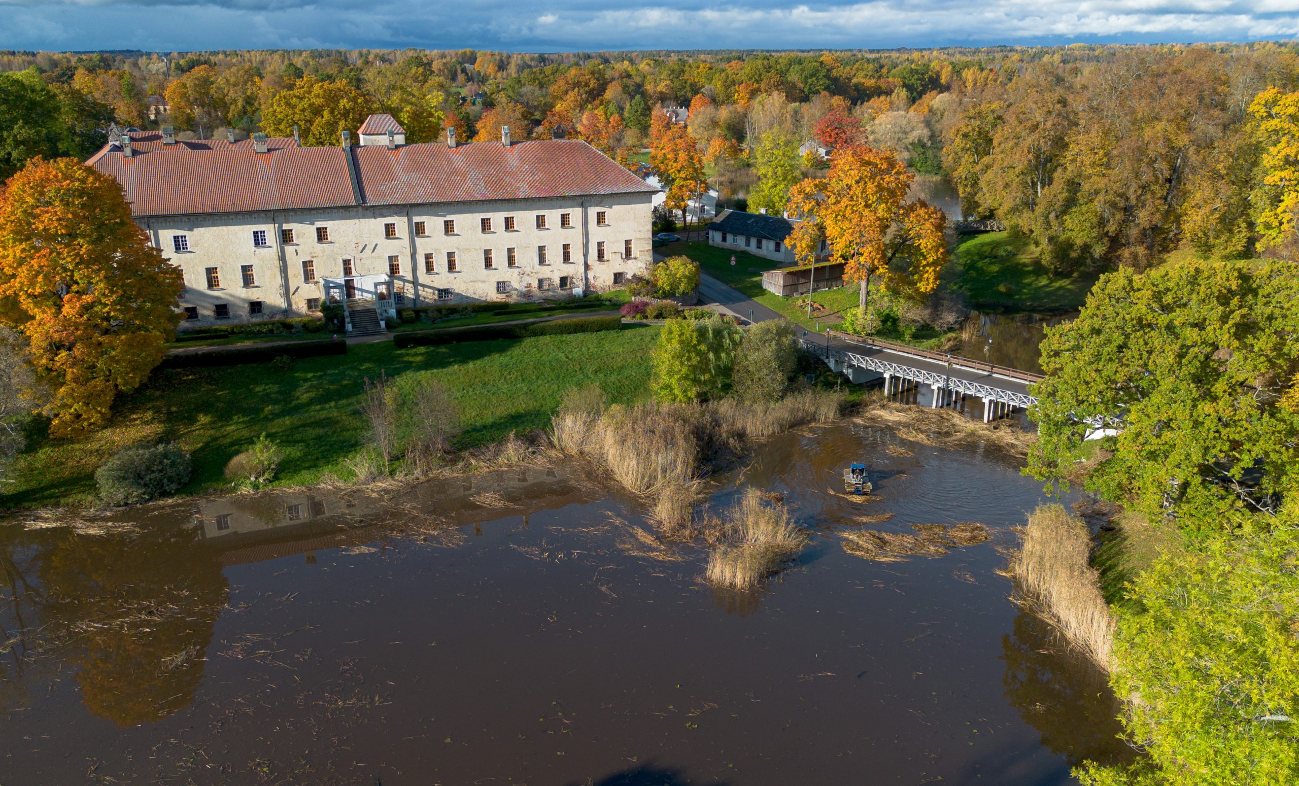 Panorāmas skats no putna lidojuma uz Dundagas pili, dīķi, rudens kokiem un tīrīšanas amfībiju.