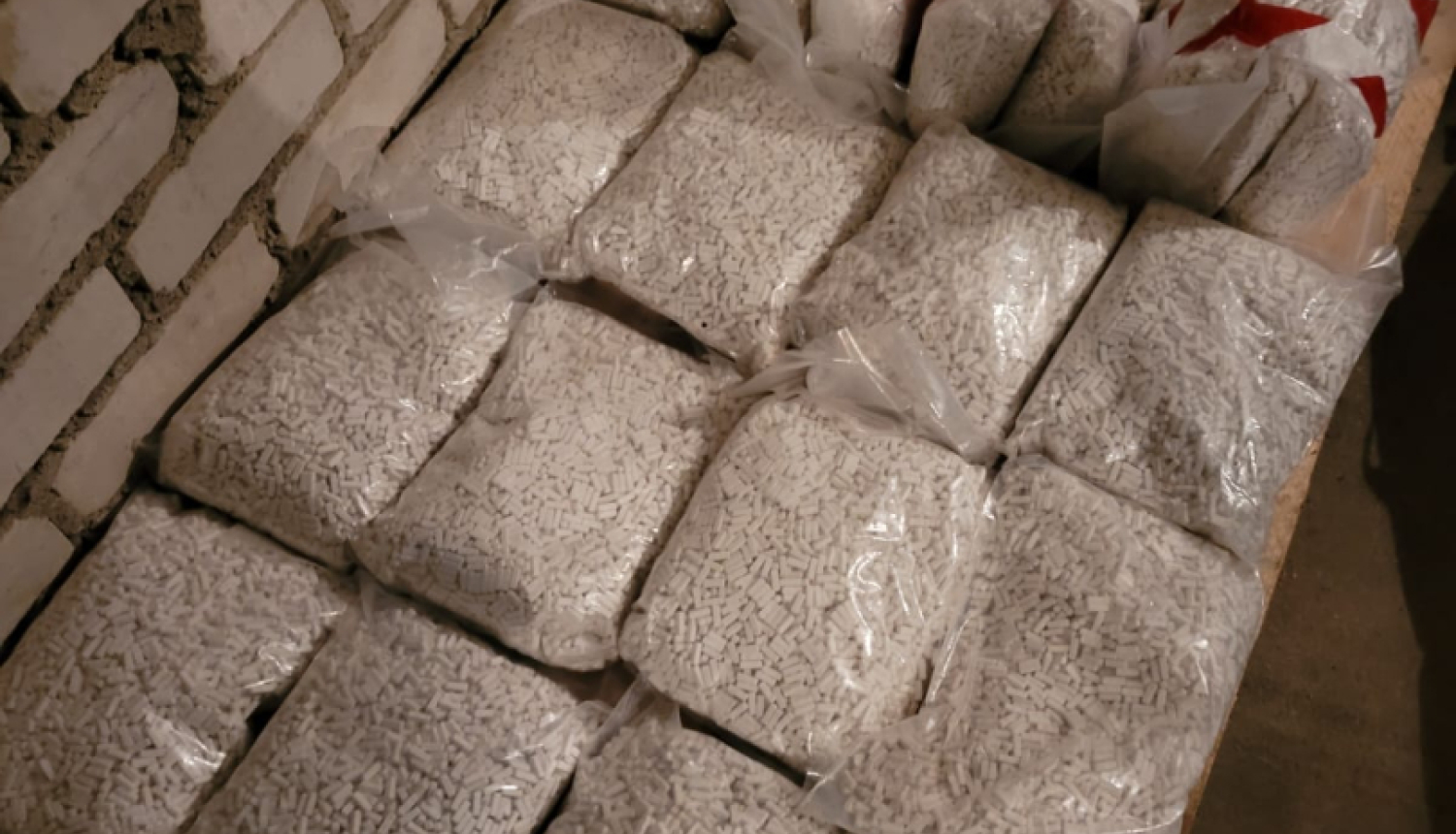 Plastmasas maisi ar granulām vai pulverveida materiālu, novietoti rindā uz grīdas pie ķieģeļu sienas.