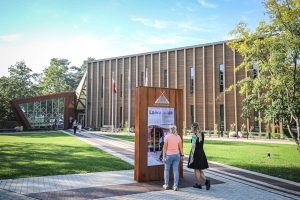 Ventspils Piejūras brīvdabas muzeja jaunā koka ēka "Laivu māja" saulainā dienā ar apmeklētājiem.