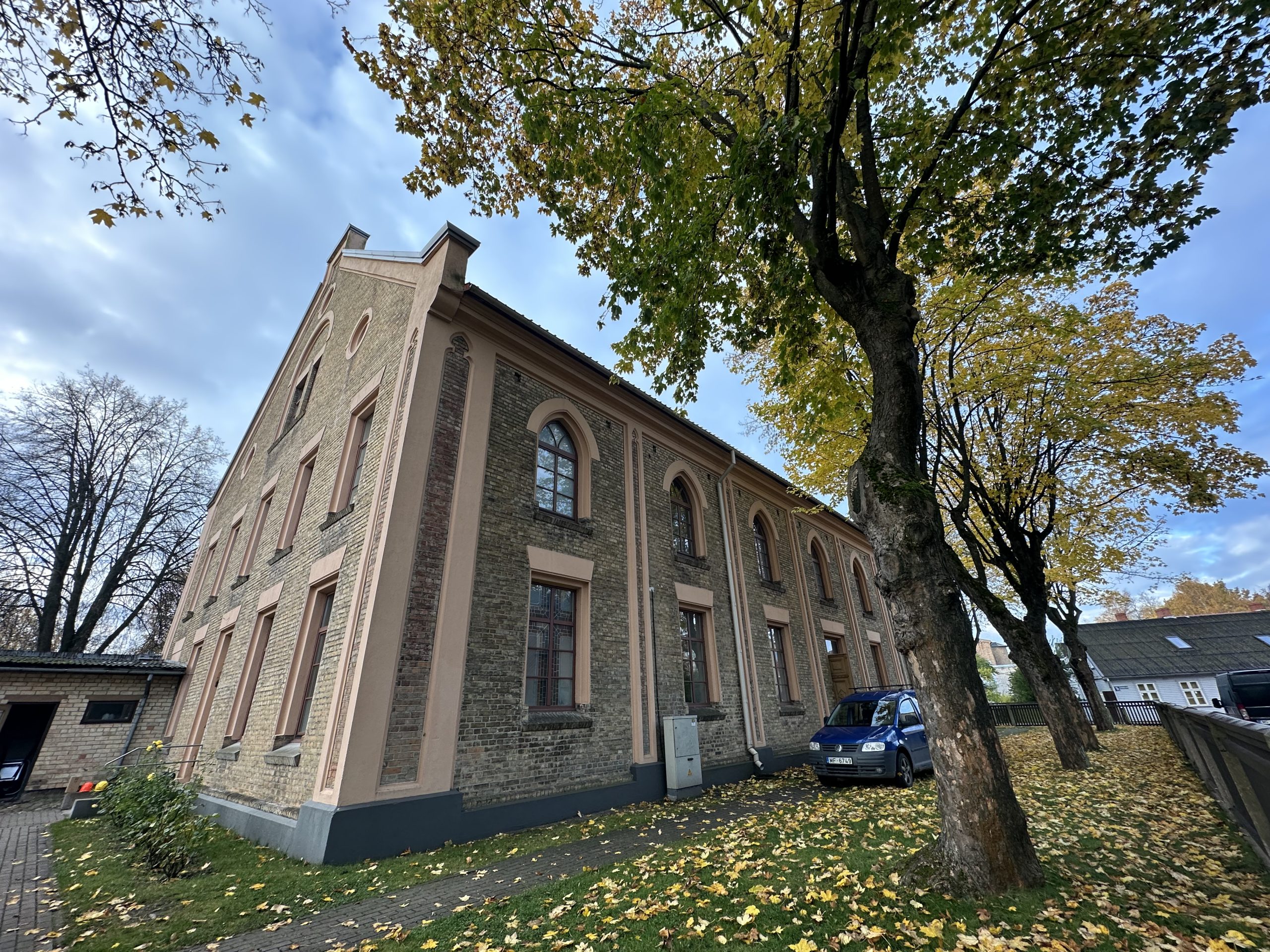 Ventspils baptistu baznīcas sānu skats rudenī, koku lapas nokritušas zemē.