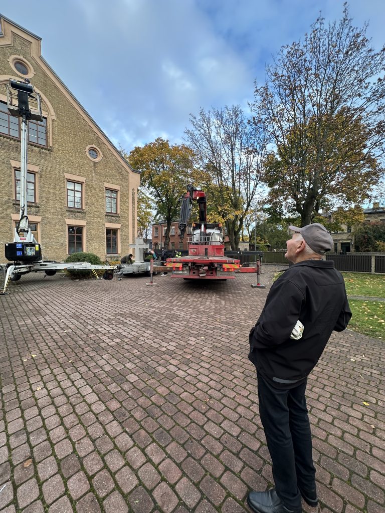 Ventspils baptistu draudzes vecākais loceklis pagalmā vēro krusta uzstādīšanas darbus.
