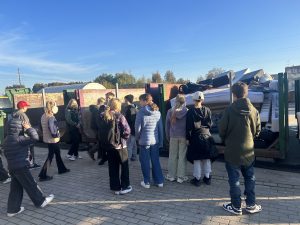 Skolēni aplūko lielgabarīta atkritumu konteinerus vides izglītības ekskursijā.