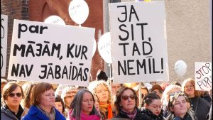 Protestētāju grupa ar diviem plakātiem, kas aicina uz drošību no vardarbības.