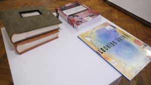 Uz galda izliktas vairākas grāmatas un albumi, tostarp mākslinieka Leonīda Āriņa katalogs.