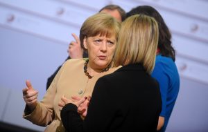 Angela Merkele sarunājas ar citu dalībnieci konferencē, oficiālā pasākuma gaisotnē.