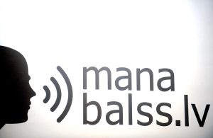 Platformas “ManaBalss.lv” logo uz baltas sienas.