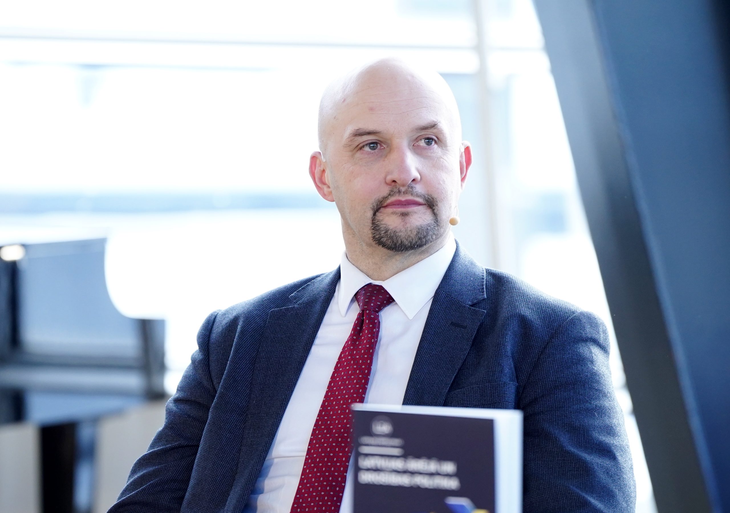 Jānis Sārts uzvalkā ar sarkanu kaklasaiti piedalās konferencē.