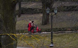 Pāris sarkanos apģērbos brauc ar sarkanu motorolleru pa parku.