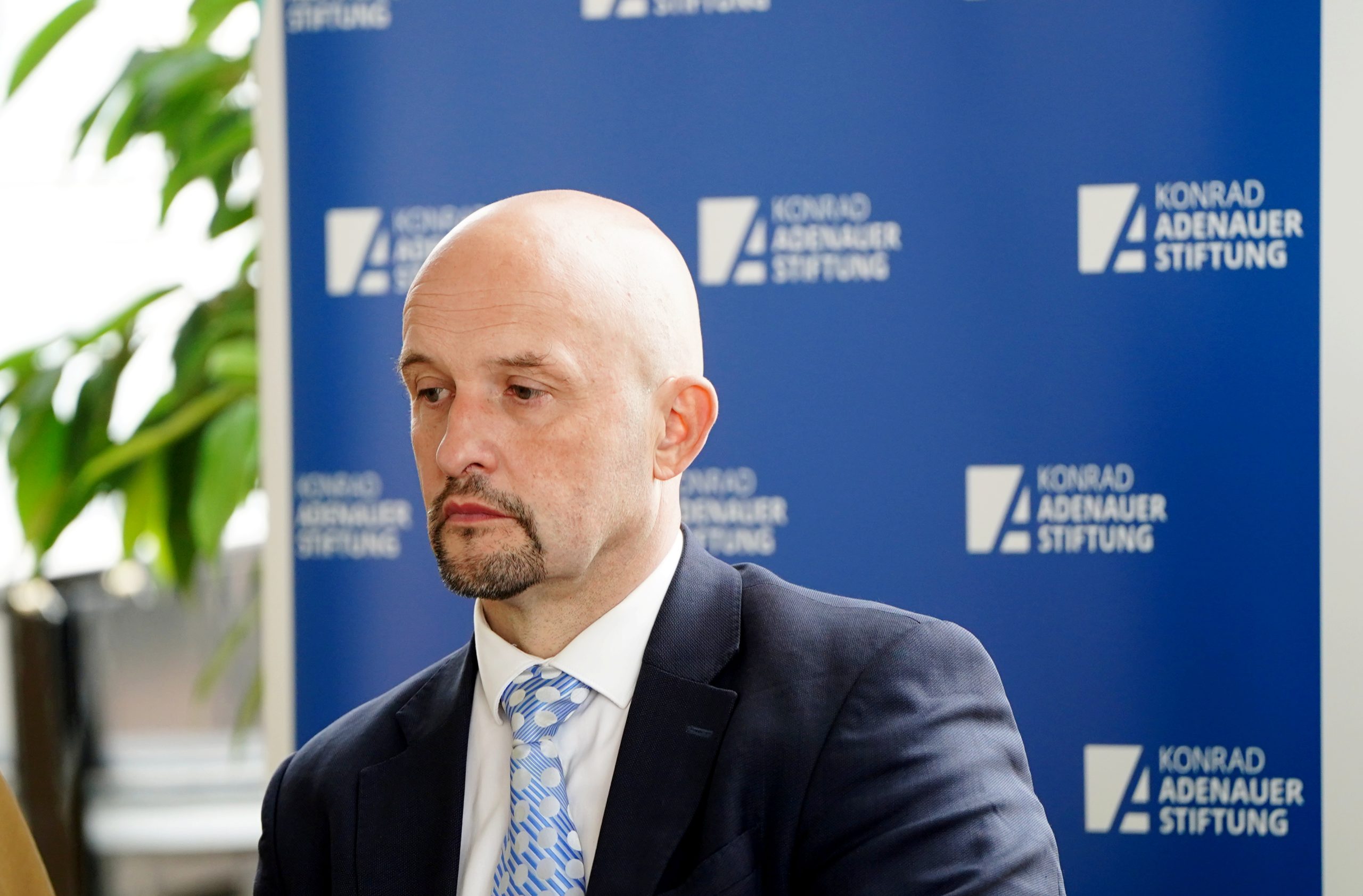 Jānis Sārts uzvalkā konferencē ar “Konrad Adenauer Stiftung” fonu.