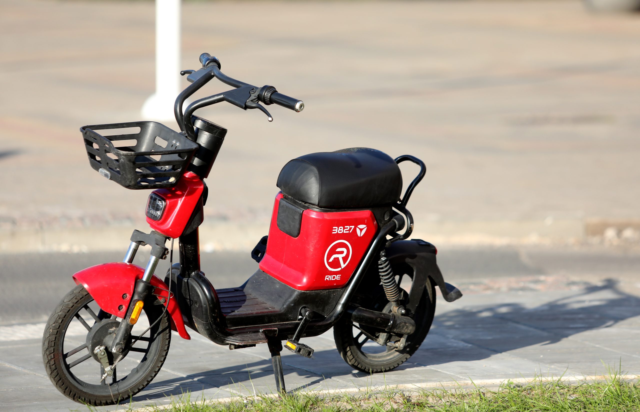 Sarkans elektriskais motorolleris ar groziņu uz ietves