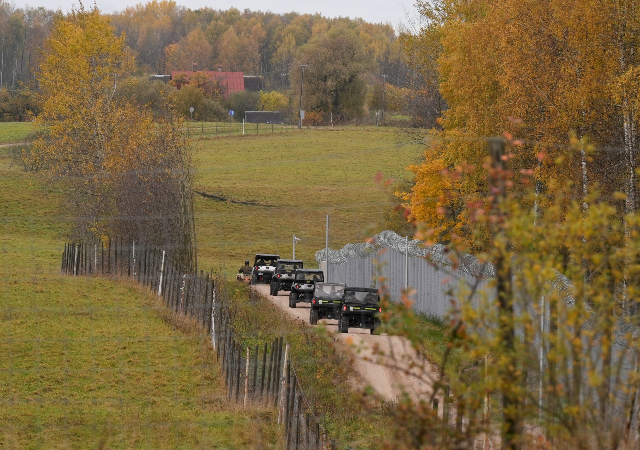Latvijas valsts robeža ar Baltkrieviju, kur redzams žogs un ceļš, pa kuru rudenīgā ainavā pārvietojas robežsardzes patruļas transportlīdzekļi.