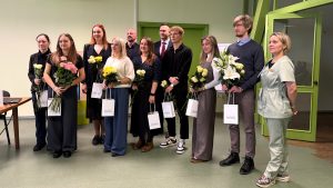 Astoņi jaunie rezidenti un absolventi, turot ziedu pušķus, pozē fotogrāfijai kopā ar vadošajiem darbiniekiem Jēkabpils reģionālajā slimnīcā.
