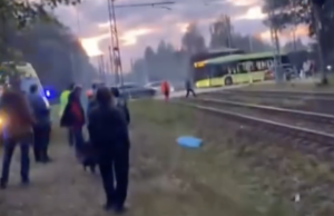 Cilvēki un sabiedriskais transports pie dzelzceļa sliedēm pēc negadījuma