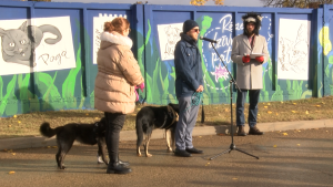 Cilvēki ar suņiem piedalās sienas ar dzīvnieku portretiem atklāšanā pie Rēzeknes dzīvnieku patversmes.