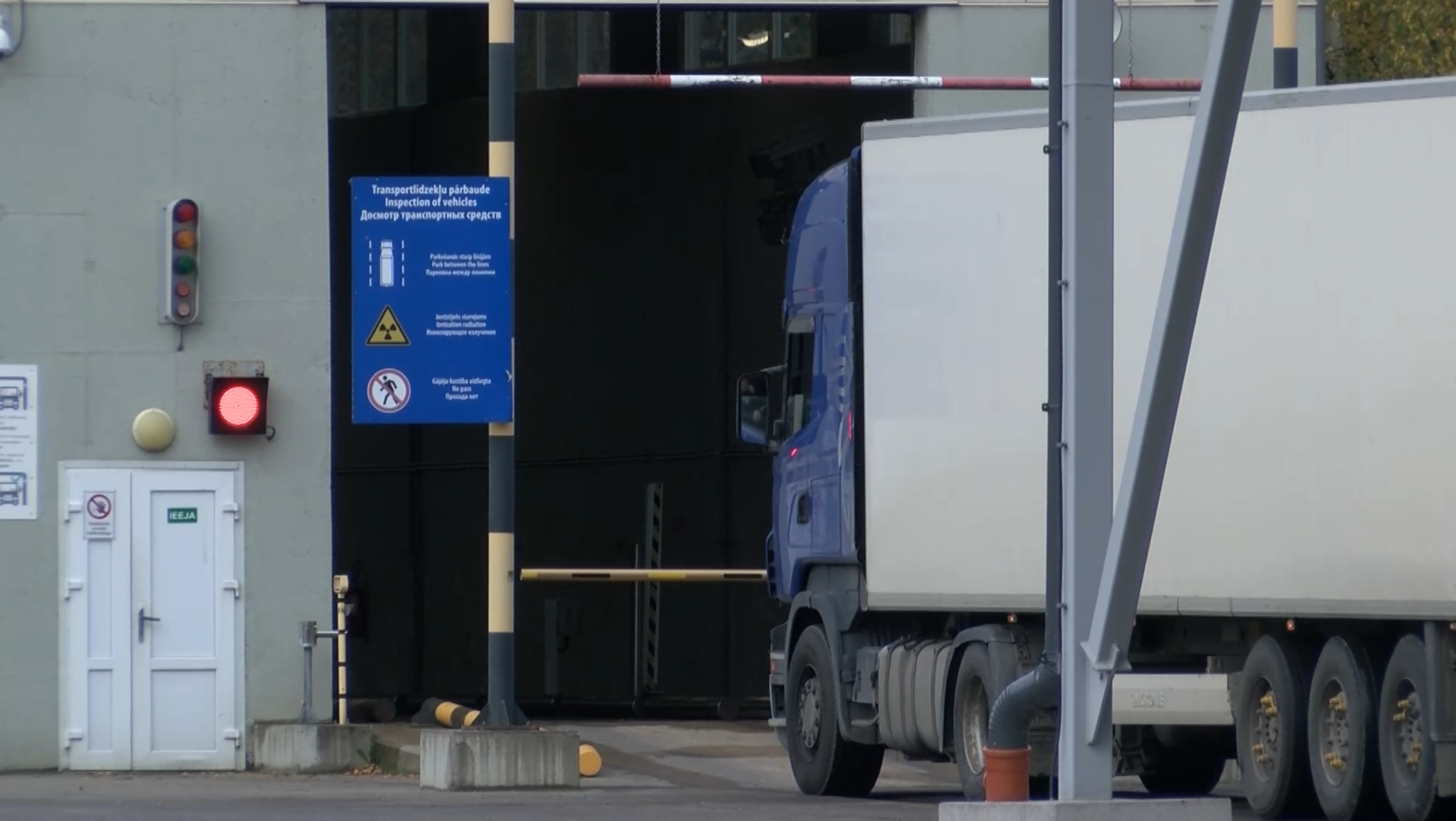 Kravas automašīna gaida pie robežkontroles pārbaudes punkta ar sarkano luksofora signālu.