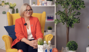Neiroloģe Linda Zvaune sarunas laikā sēž dzeltenā krēslā gaišā telpā ar augiem un galda priekšmetiem.