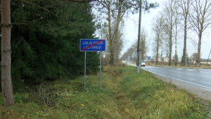 Ceļazīme ar uzrakstu “Lielie Dreizi / Lelī Dreizi” pie ceļa, kas ved cauri kokiem